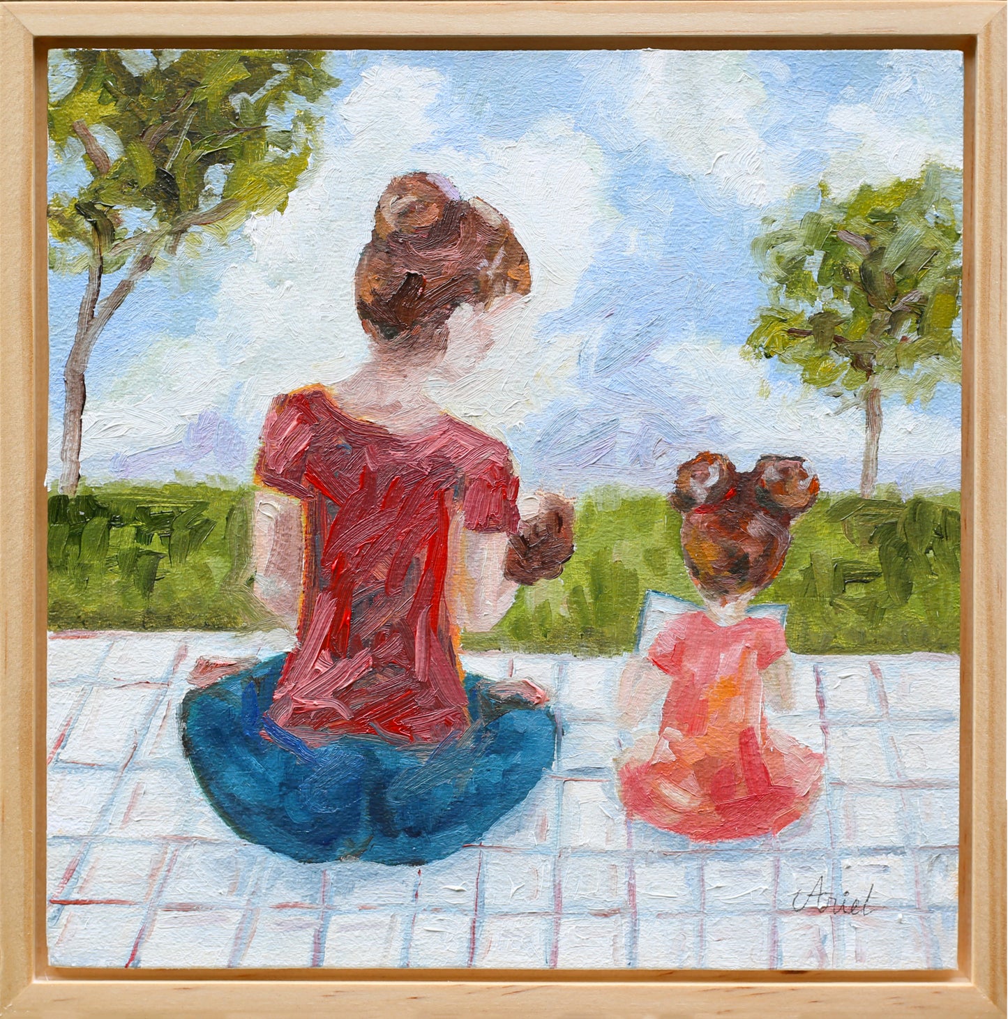 Impressionist-style painting of a woman and young girl sitting on a picnic blanket, viewed from behind. The woman wears a red top and blue pants, while the girl wears a pink dress. Both have their hair in buns as they sit side by side, looking out toward a grassy field with trees and a bright blue sky. The brushstrokes are loose and textured, creating a warm, tender atmosphere.